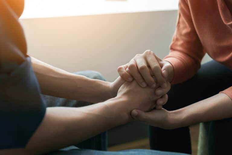An empathetic therapist and patient holding hands as they discuss a tough issue.