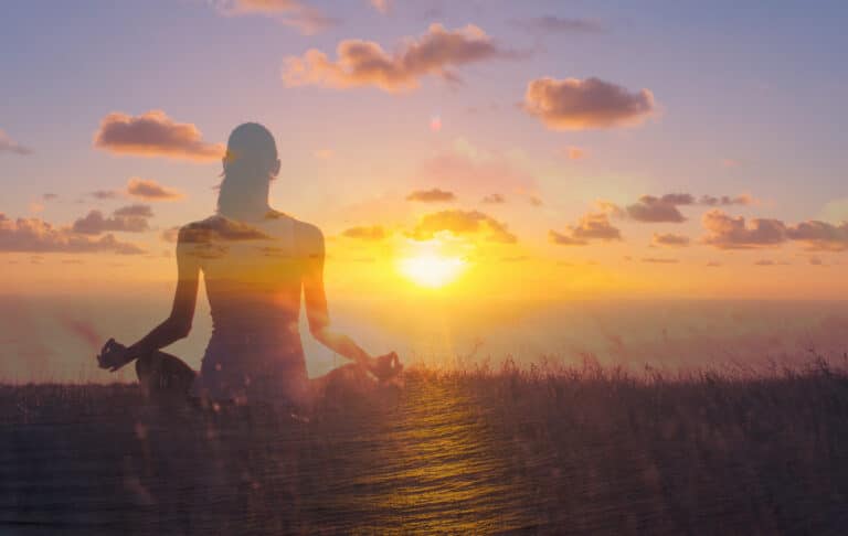 Woman meditating at a beautiful sunrise in calm state of mind.